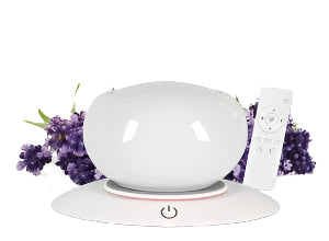 Curved Absolute Essential Diffuser on table with Handheld Remote and Floral Bunch in background.